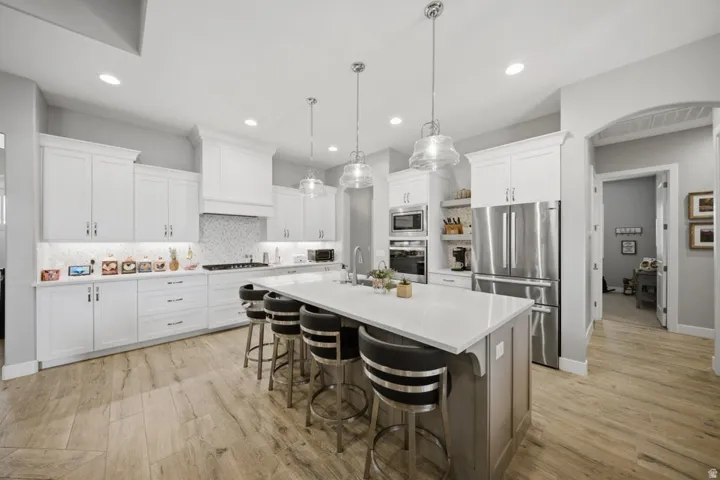 Two tone kitchen featuring stainless steel appliances, a center island with sink, a breakfast bar, tasteful backsplash, and pendant lighting