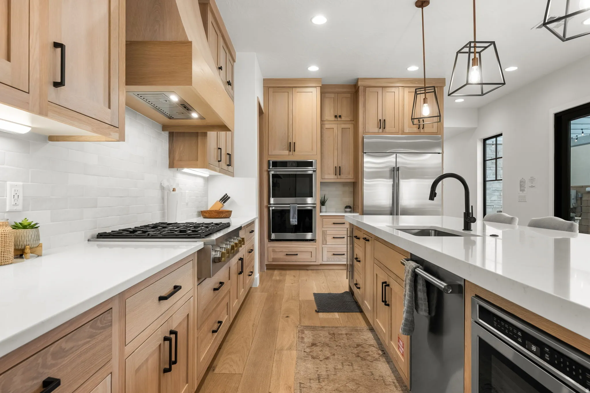 Kitchen featuring light stone counters, light wood finished floors, stainless steel appliances, pendant lighting, and light wood finish cabinets