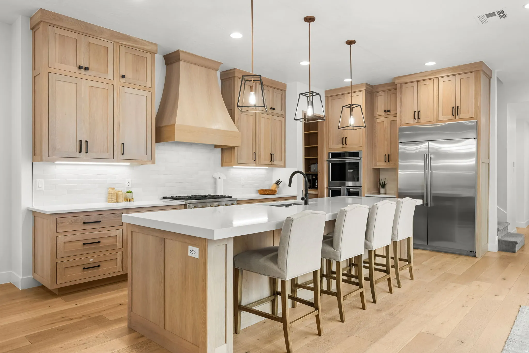 Kitchen featuring stainless steel appliances, decorative backsplash, a kitchen island with sink, a breakfast bar area, and light wood finished floors