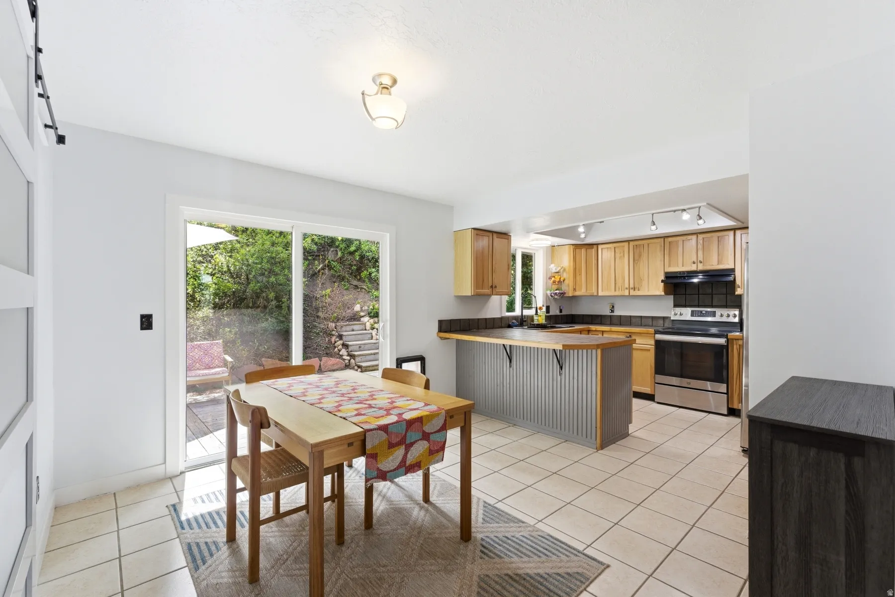 Kitchen with a peninsula, light tile patterned flooring, electric stove, a breakfast bar, and track lighting