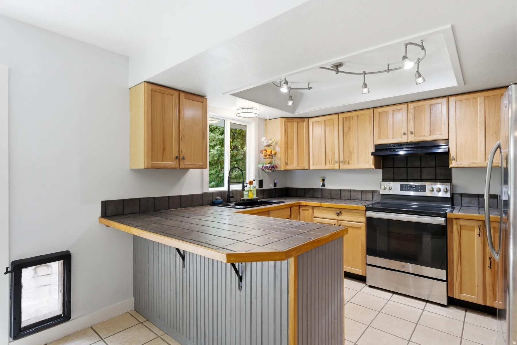 Kitchen with a breakfast bar, stainless steel appliances, a peninsula, light tile patterned floors, and light wood finish cabinetry