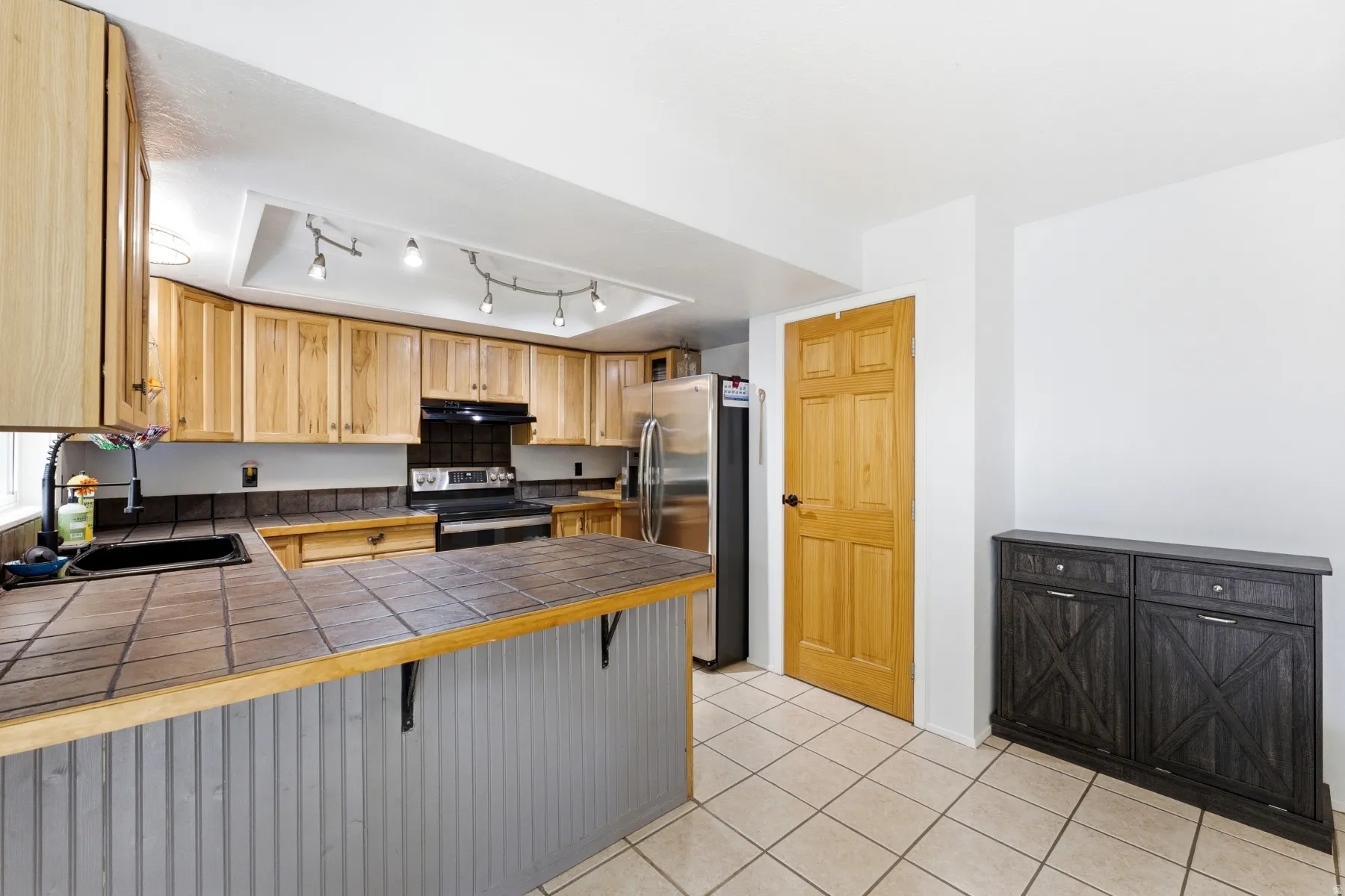 Kitchen featuring stainless steel appliances, a breakfast bar, tile countertops, a peninsula, and light tile patterned floors