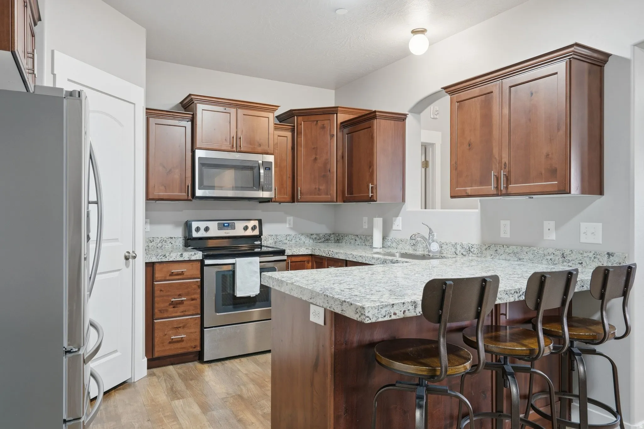 Kitchen with stainless steel appliances, a peninsula, a kitchen breakfast bar, light wood-style floors, and wood finish cabinetry