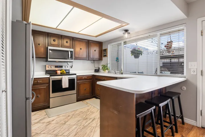 Kitchen featuring stainless steel appliances, a peninsula, light countertops, a breakfast bar, and dark wood finish cabinetry