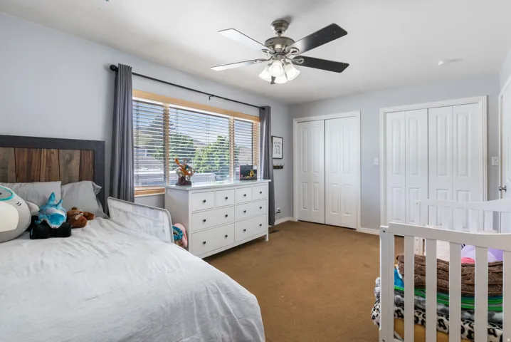 Bedroom with two closets, dark colored carpet, and a ceiling fan