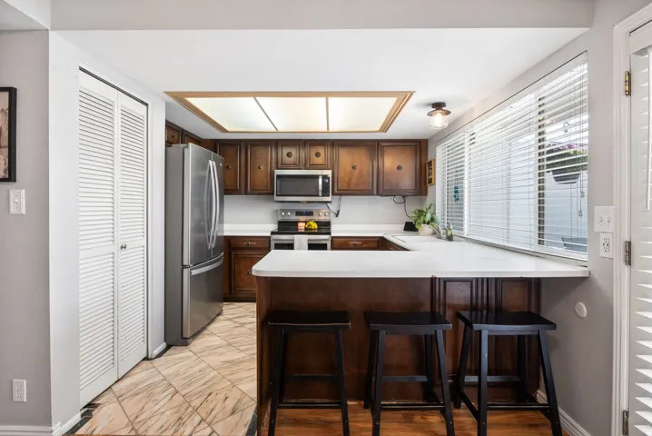 Kitchen with light countertops, a breakfast bar area, a peninsula, stainless steel appliances, and dark wood finish cabinetry