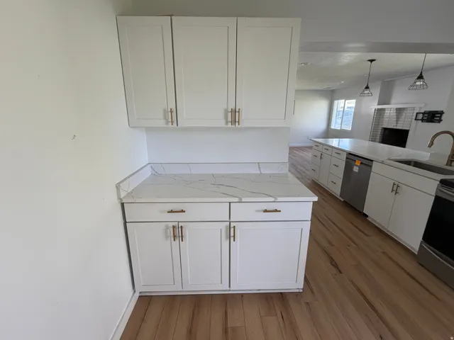 Kitchen with white cabinetry, light wood-style flooring, pendant lighting, and light stone countertops