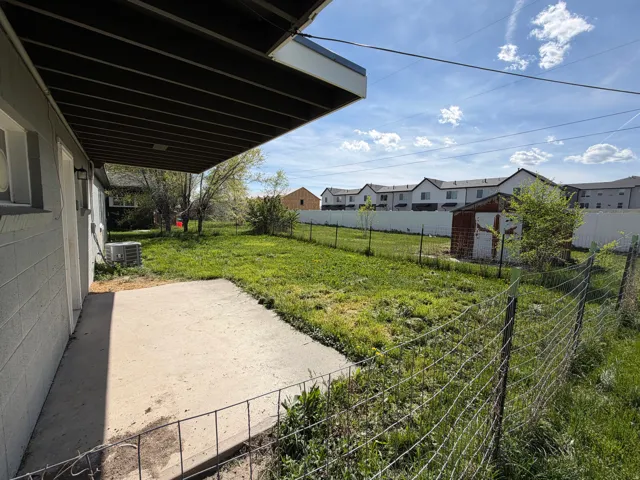 Fenced backyard with a patio area, a residential view, and a storage unit
