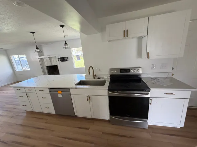 Kitchen with stainless steel appliances, white cabinets, a peninsula, dark wood-type flooring, and light stone countertops