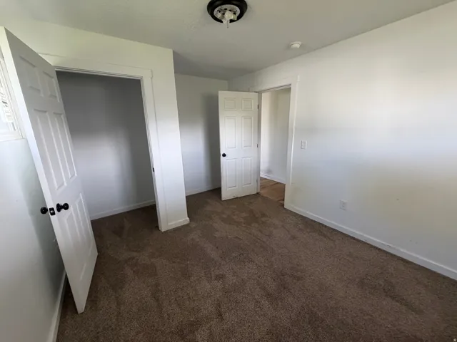Unfurnished bedroom with dark colored carpet and baseboards