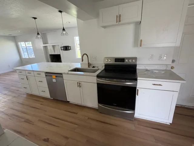 Kitchen with a peninsula, stainless steel appliances, white cabinets, light wood finished floors, and a textured ceiling