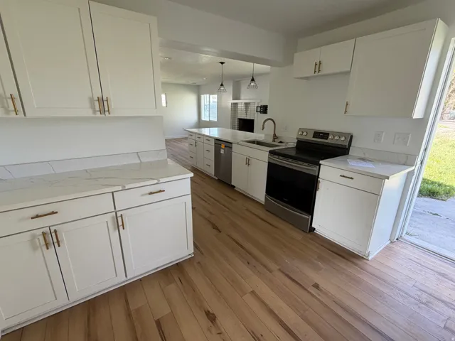Kitchen with white cabinets, stainless steel appliances, light wood-style flooring, hanging light fixtures, and light stone counters