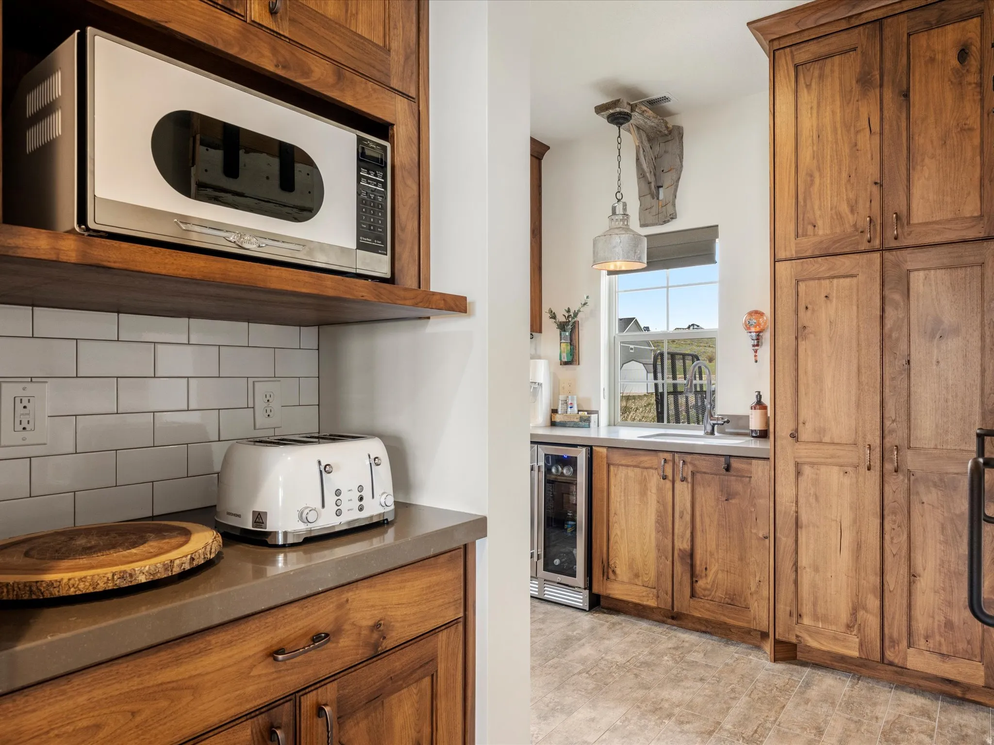 Kitchen featuring wood finish cabinets, white microwave, backsplash, wine cooler, and hanging light fixtures