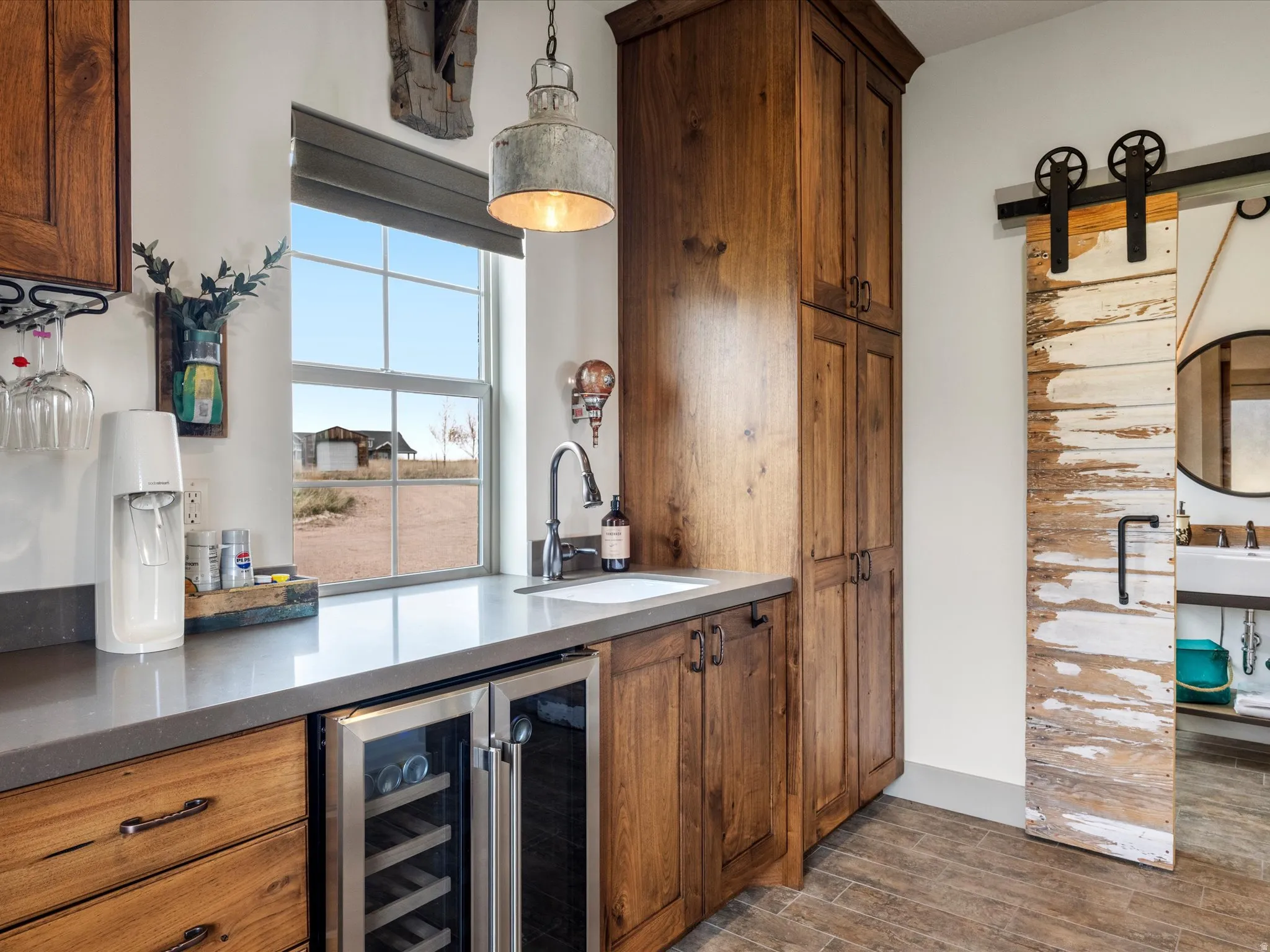 Bar with wood finish floors, beverage cooler, a barn door, wood finish cabinets, and decorative light fixtures
