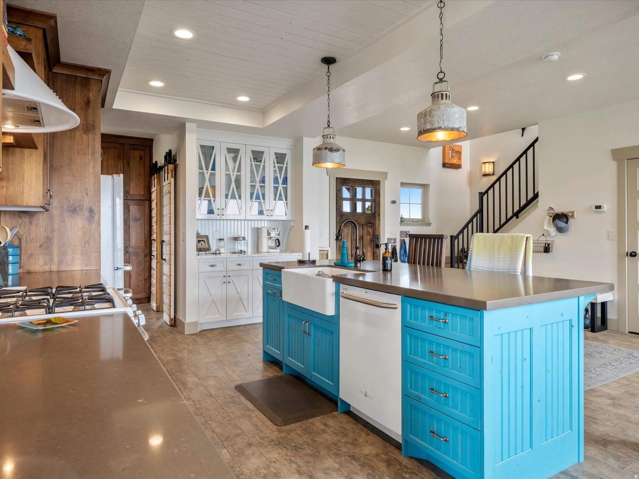 Two tone kitchen with dual tone cabinets, glass insert cabinets, a center island with sink, hanging light fixtures, and light wood-style flooring