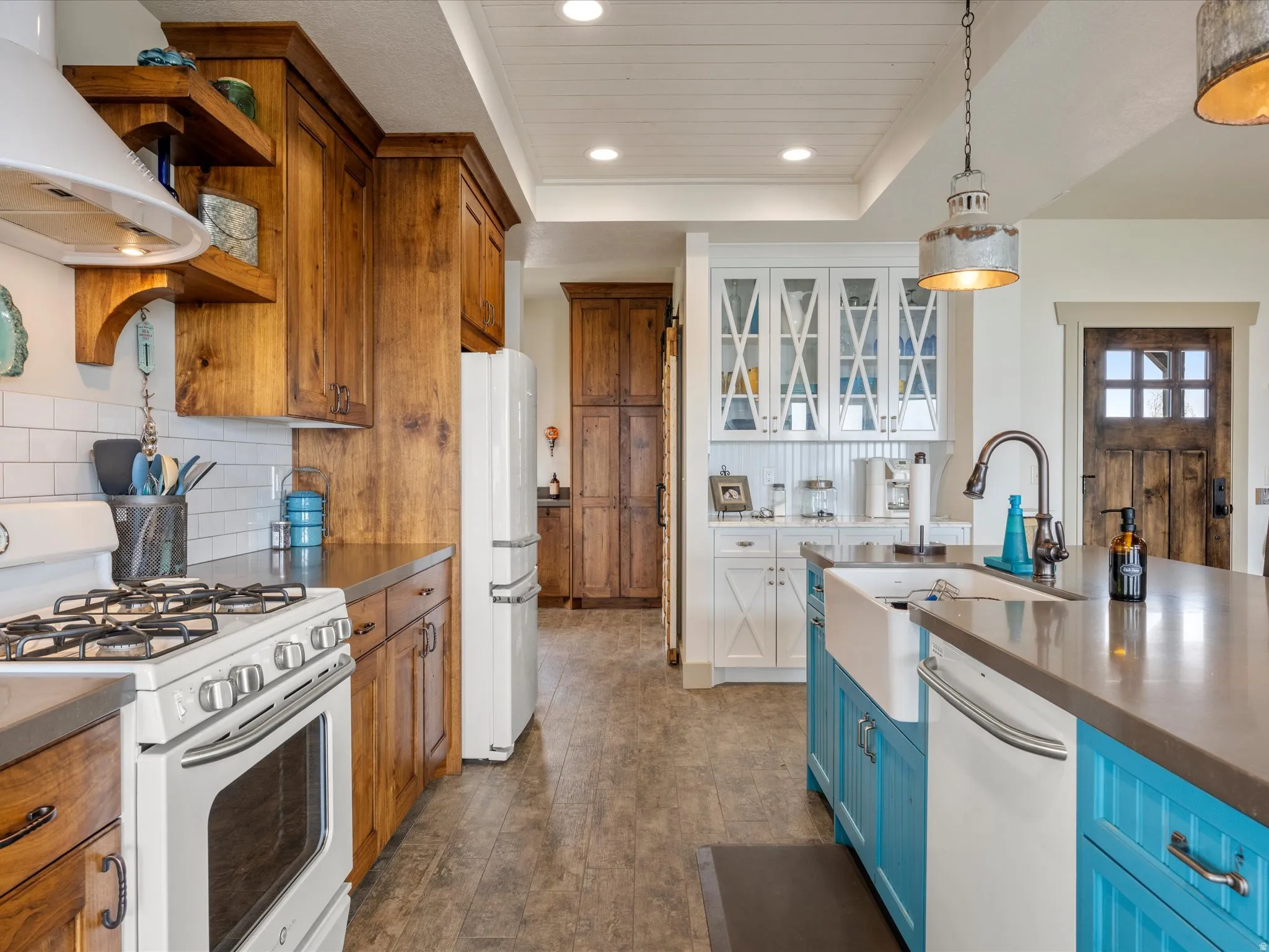 Dual tone kitchen with two tone color scheme, white appliances, glass fronted cabinets, exhaust hood, and dark wood-style floors