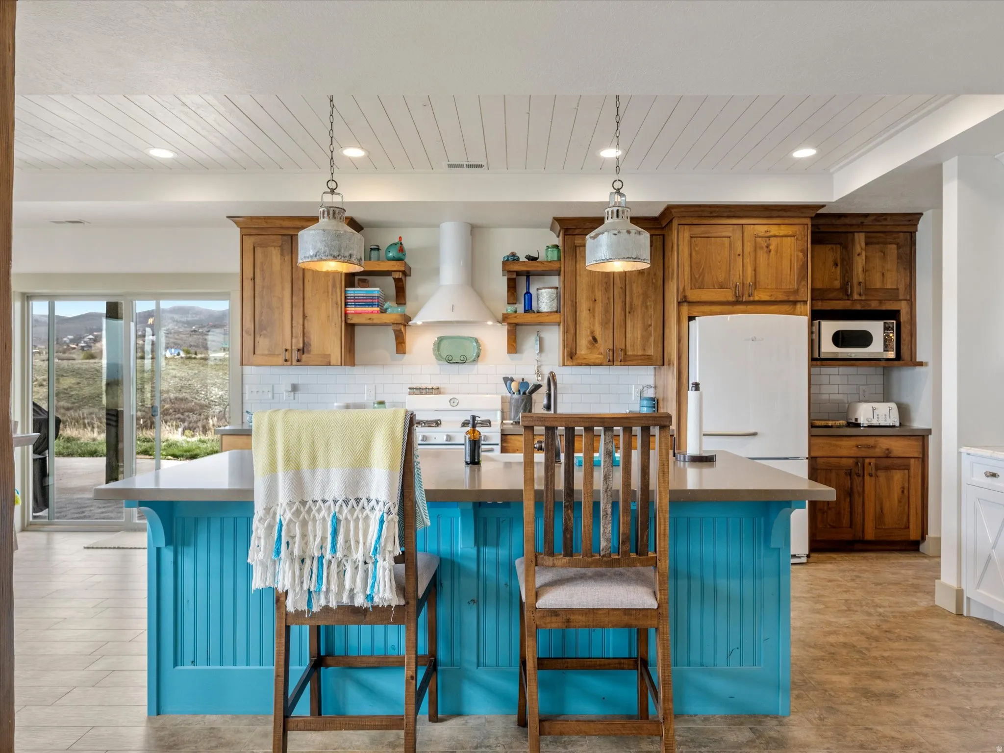 Kitchen with a breakfast bar area, two tone color scheme, white appliances, open shelves, and a kitchen island with sink
