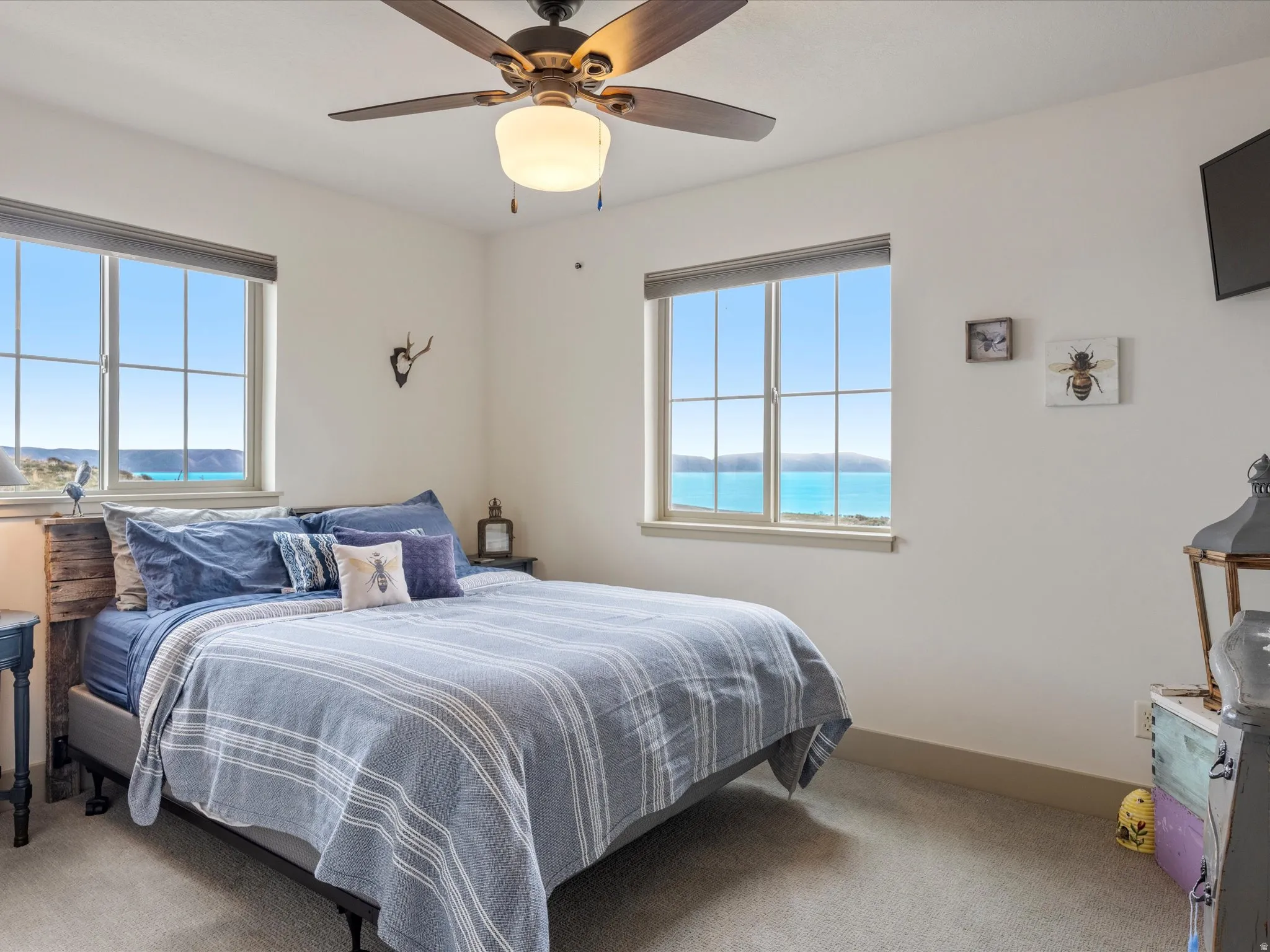 Bedroom with light carpet, a ceiling fan, multiple windows, and a water view