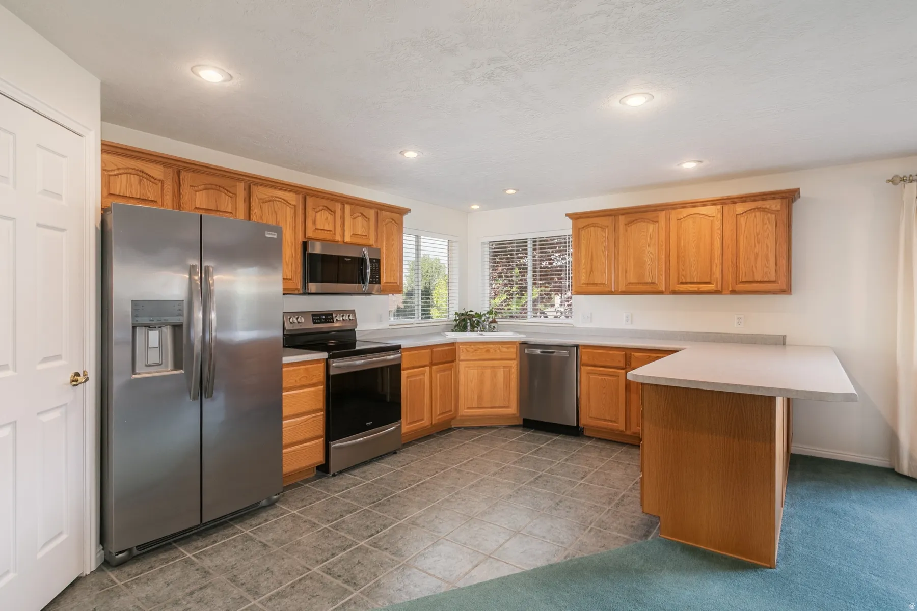 Kitchen with a peninsula, stainless steel appliances, light countertops, wood finish cabinetry, and recessed lighting