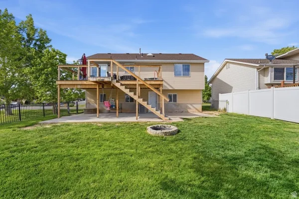 Back of property with a fenced backyard, a deck, an outdoor fire pit, and a patio