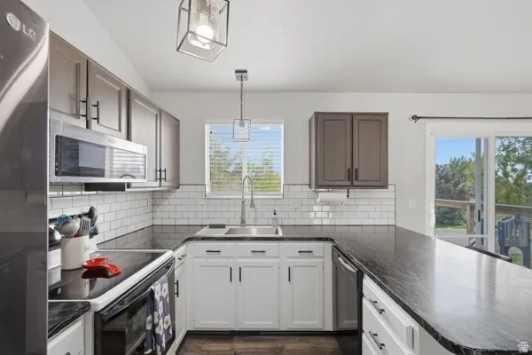 Kitchen featuring stainless steel appliances, a peninsula, pendant lighting, dark stone countertops, and dark wood-style floors
