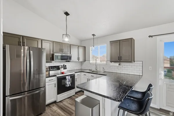 Kitchen featuring stainless steel appliances, a peninsula, a breakfast bar area, dark wood-style floors, and lofted ceiling