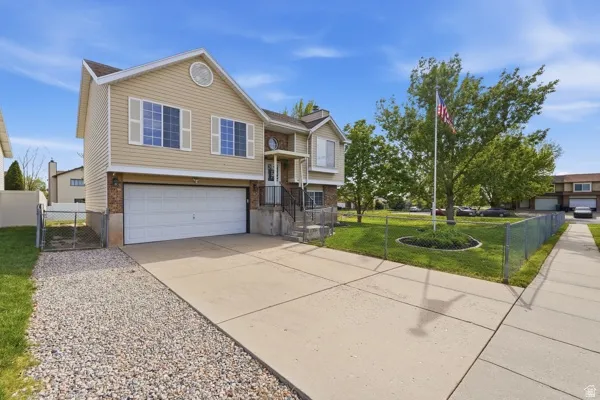 Raised ranch featuring a gate, concrete driveway, an attached garage, and brick siding