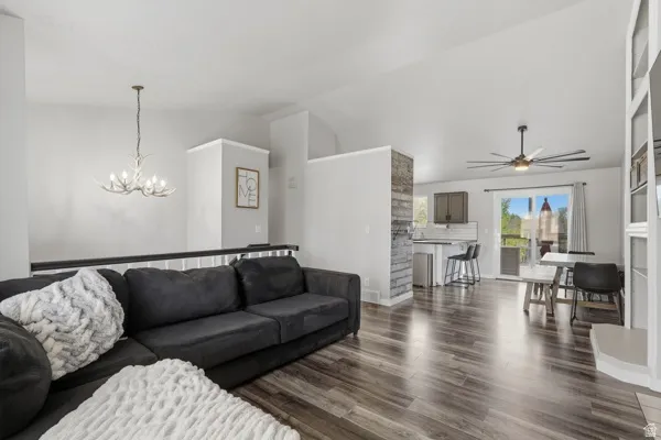 Living room with dark wood-type flooring, lofted ceiling, suspended lighting, and a ceiling fan