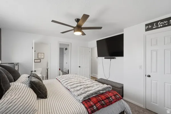 Carpeted bedroom with ensuite bath and ceiling fan