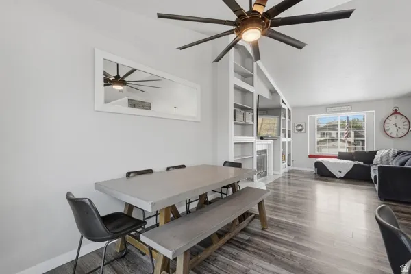 Dining area featuring a fireplace with flush hearth, ceiling fan, lofted ceiling, dark wood-style floors, and built in features
