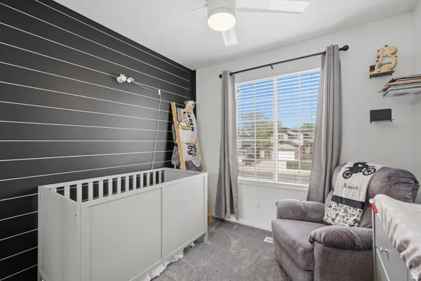 Carpeted bedroom featuring a crib, ceiling fan, and an accent wall