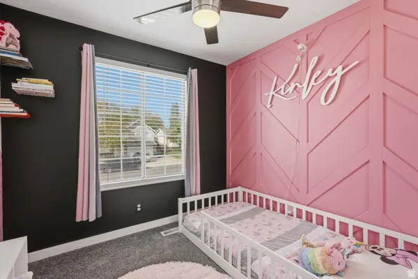 Bedroom featuring a ceiling fan, dark carpet, an accent wall, and a crib