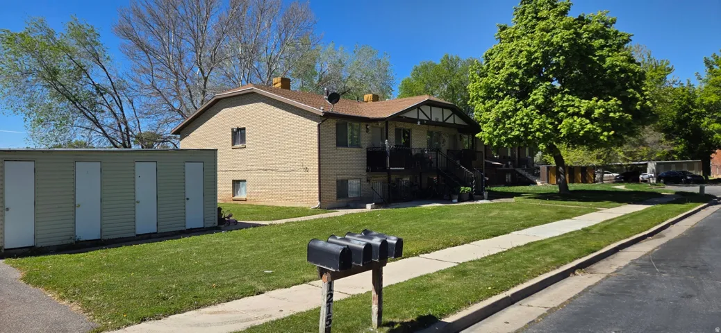 View of front of property with a front lawn, a chimney, brick siding, and a storage shed
