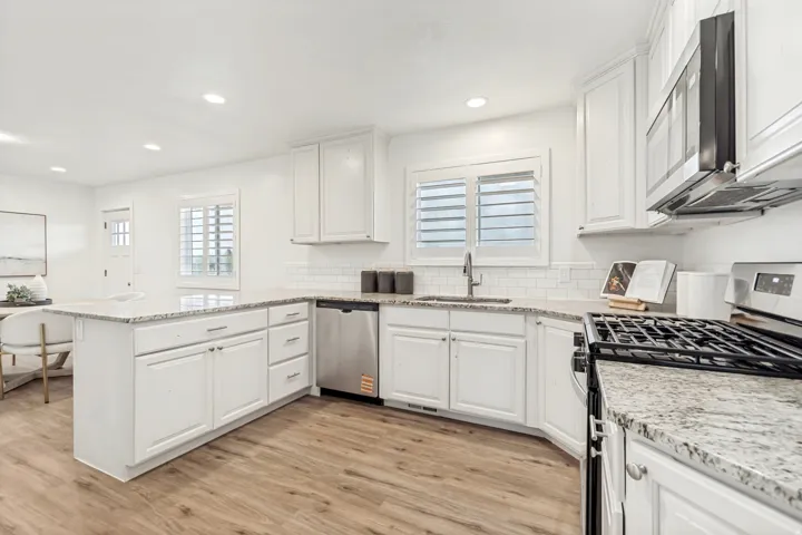 Kitchen featuring stainless steel appliances, light stone counters, a peninsula, light wood finished floors, and white cabinets