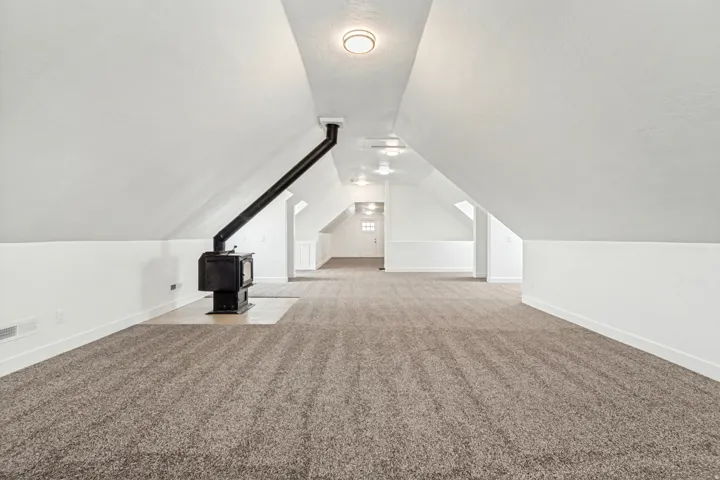 Bonus room featuring light carpet and a wood stove