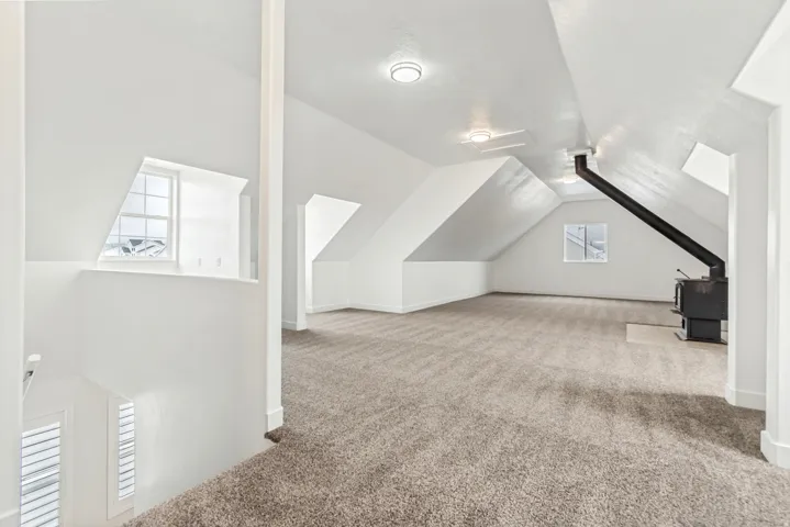 Bonus room featuring vaulted ceiling, light carpet, and a wood stove