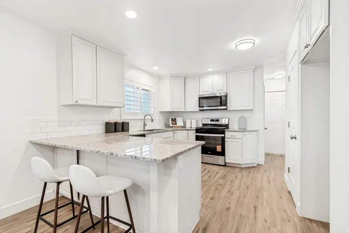 Kitchen featuring a peninsula, a kitchen breakfast bar, light wood-style floors, white cabinetry, and recessed lighting