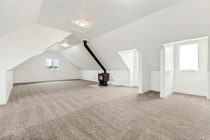 Bonus room featuring light colored carpet, vaulted ceiling, and a wood stove