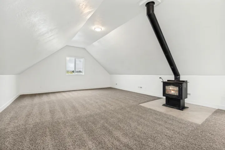 Additional living space with light colored carpet and a wood stove