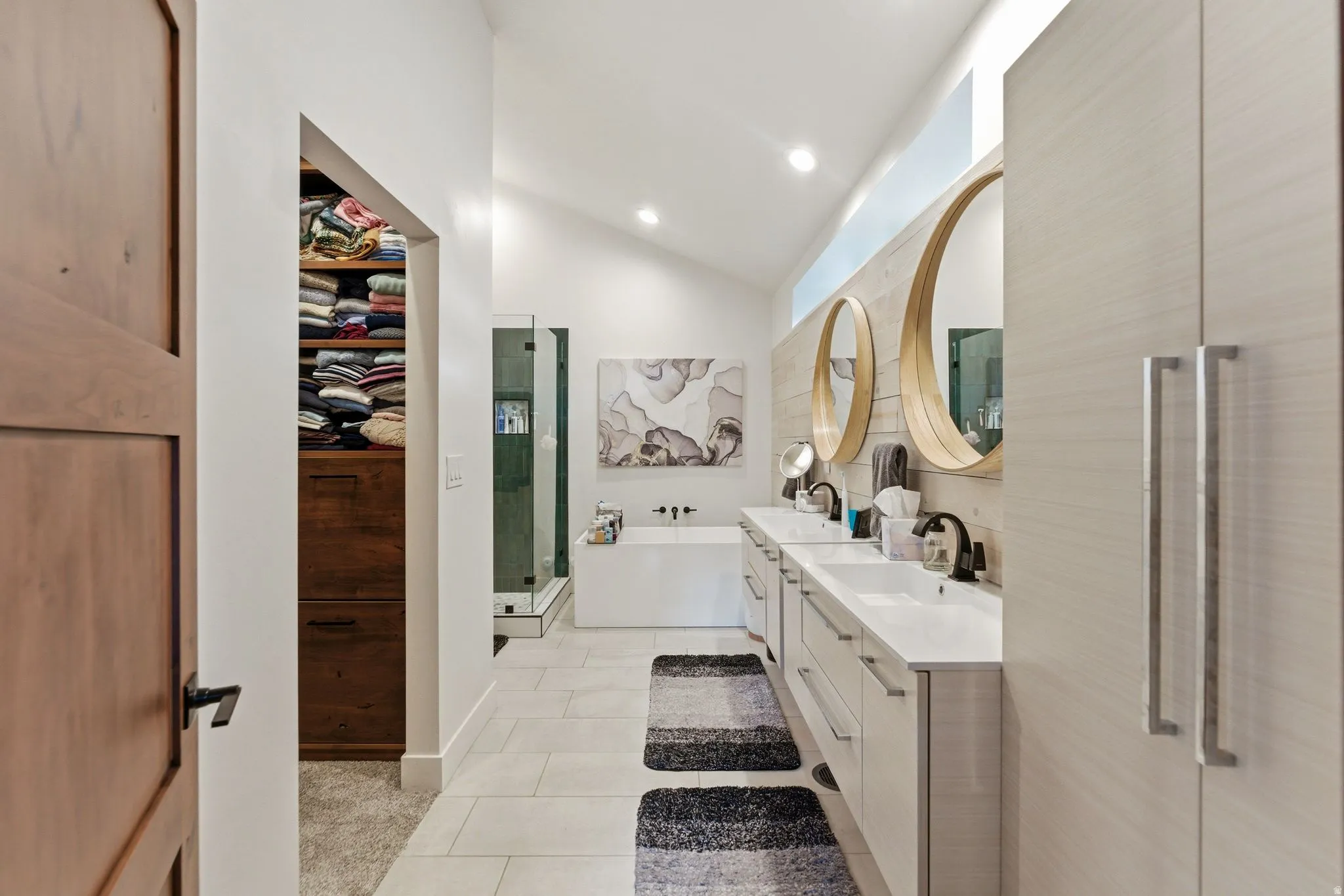 Bathroom with double vanity, vaulted ceiling, a bath, light tile patterned floors, and a shower stall