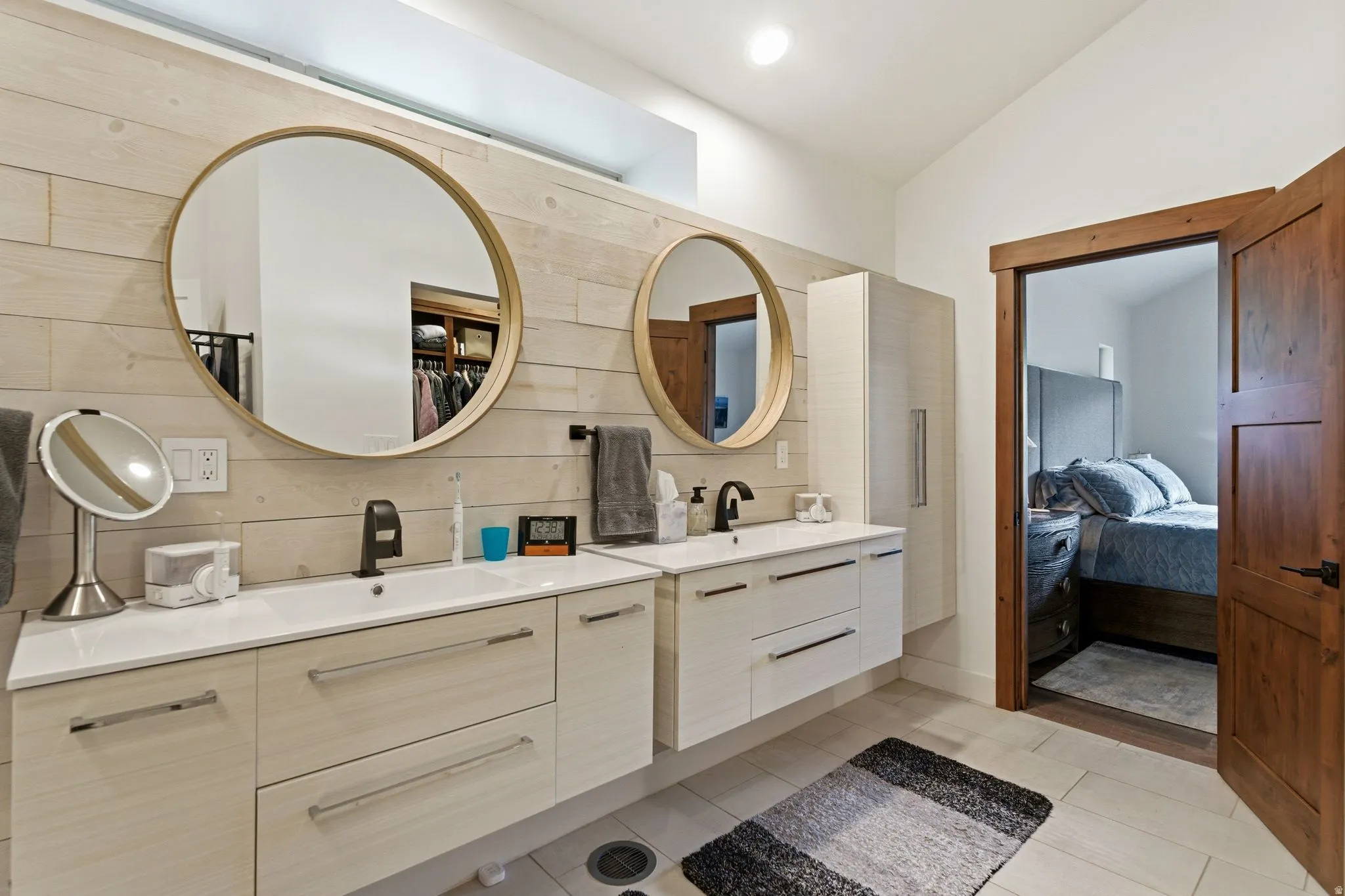 Ensuite bathroom with two vanities, lofted ceiling, light tile patterned floors, and decorative backsplash