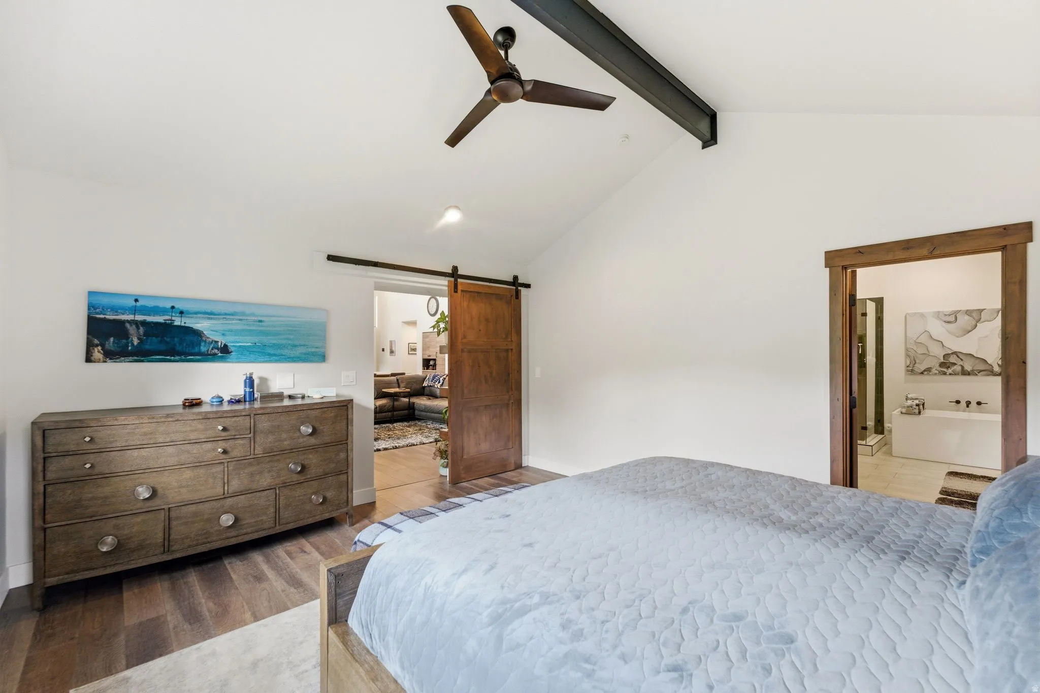 Bedroom featuring a barn door, dark wood-style flooring, beamed ceiling, ceiling fan, and connected bathroom