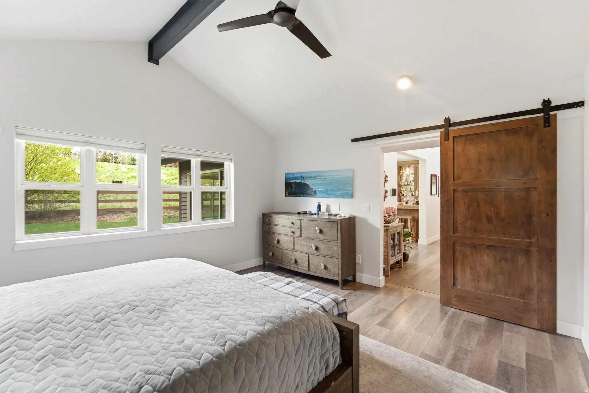 Bedroom with wood finished floors, a barn door, a ceiling fan, and beamed ceiling