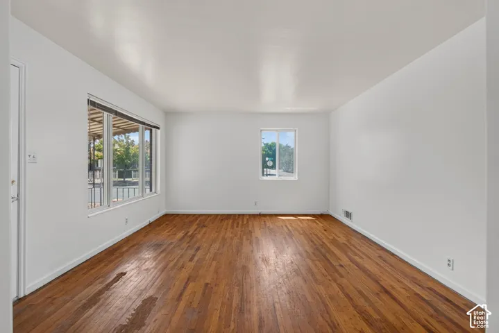 Expansive room featuring rich wood flooring, white walls, and bright natural light from multiple windows