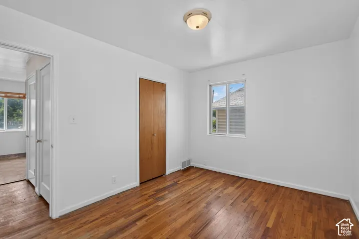 Hardwood flooring, crisp white walls, a single window, and a flush-mount ceiling light fixture define this room
