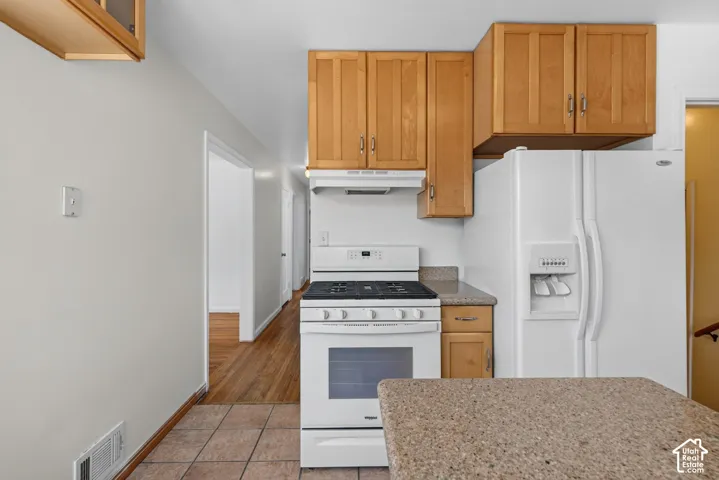 Galley kitchen featuring light wood-finish cabinetry, white appliances, and a tile floor