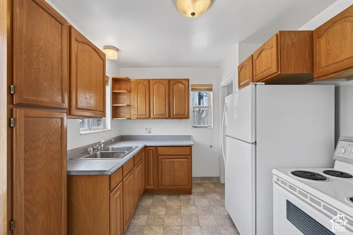 Kitchen featuring wood-finish cabinetry, a double basin stainless steel sink, light-toned countertops, and vinyl tile flooring
