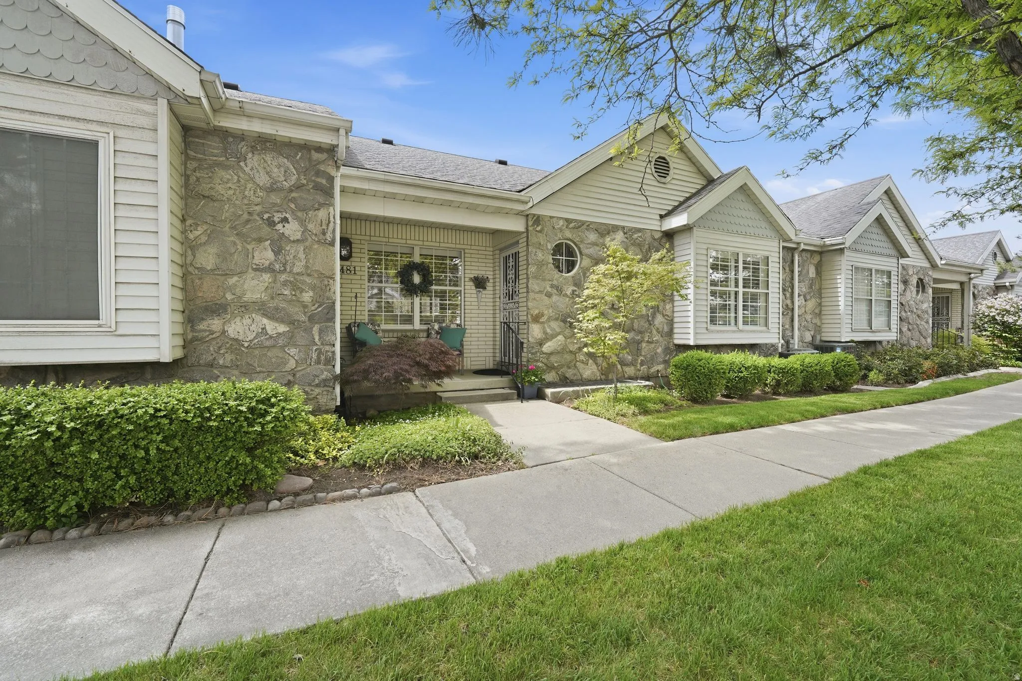 Ranch-style house featuring stone siding, a front yard, a shingled roof, and a porch