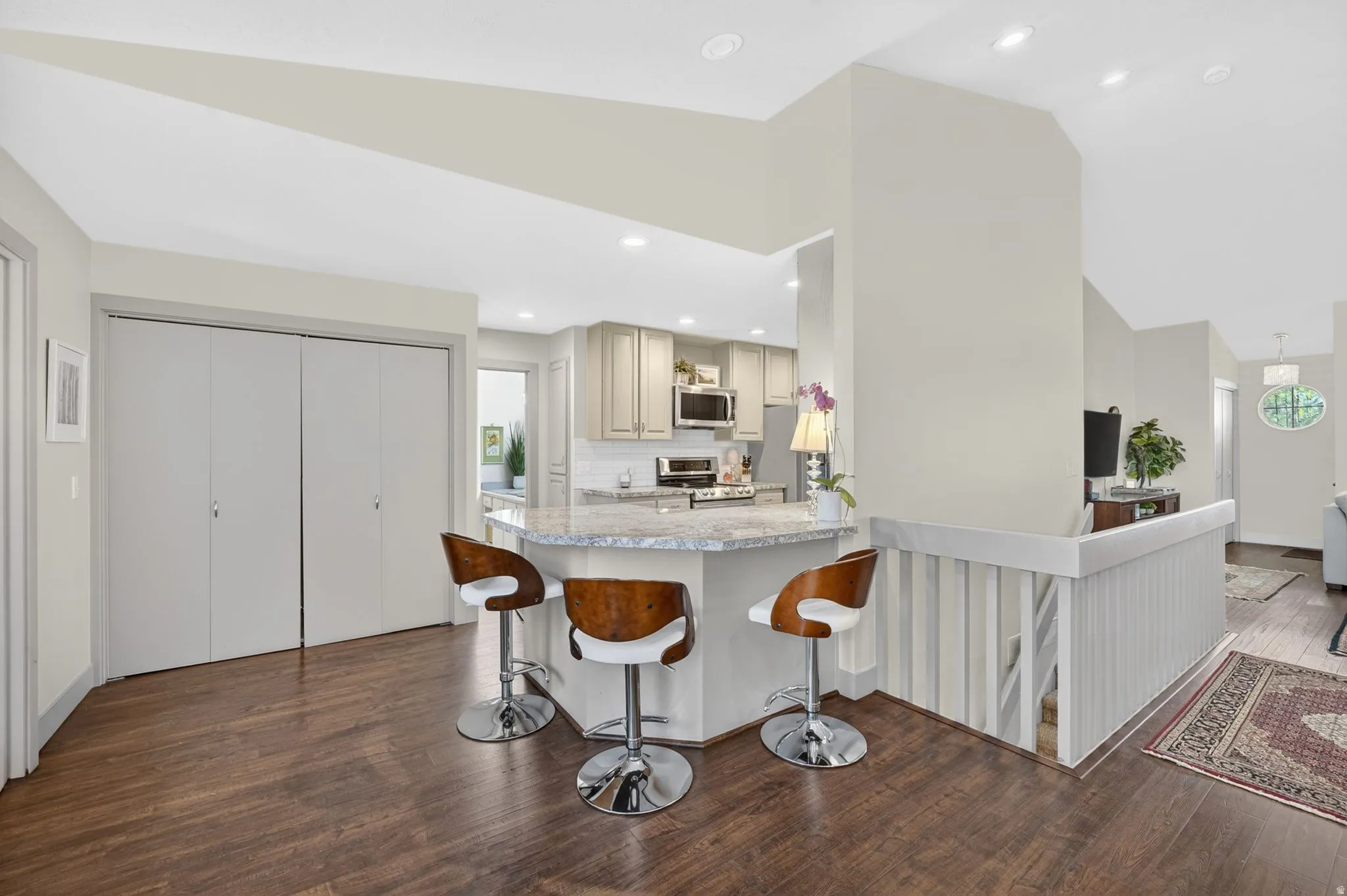 Kitchen featuring a kitchen breakfast bar, dark wood-type flooring, light stone counters, stainless steel appliances, and lofted ceiling