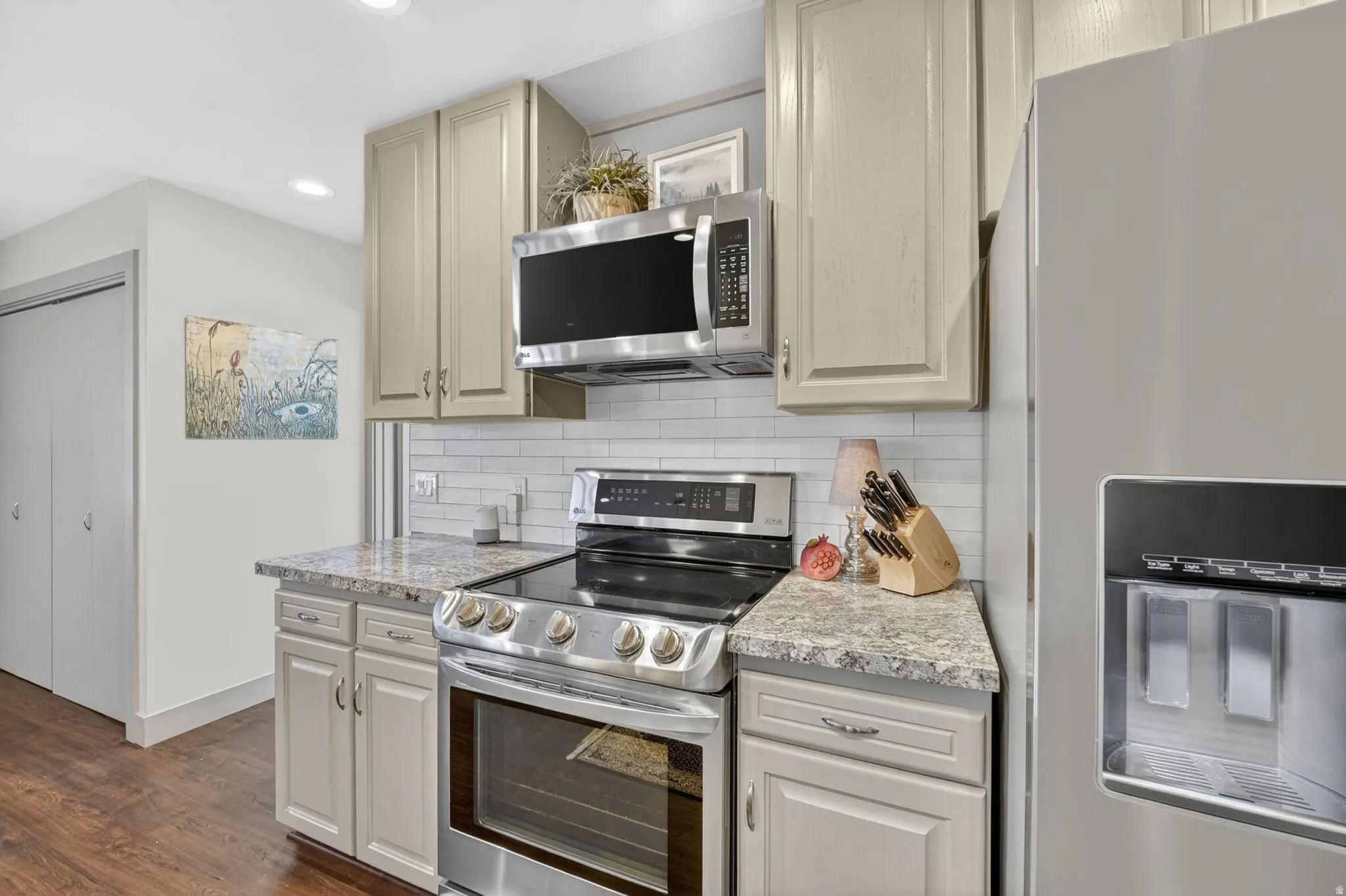 Kitchen featuring stainless steel appliances, dark wood-style flooring, recessed lighting, light stone counters, and decorative backsplash